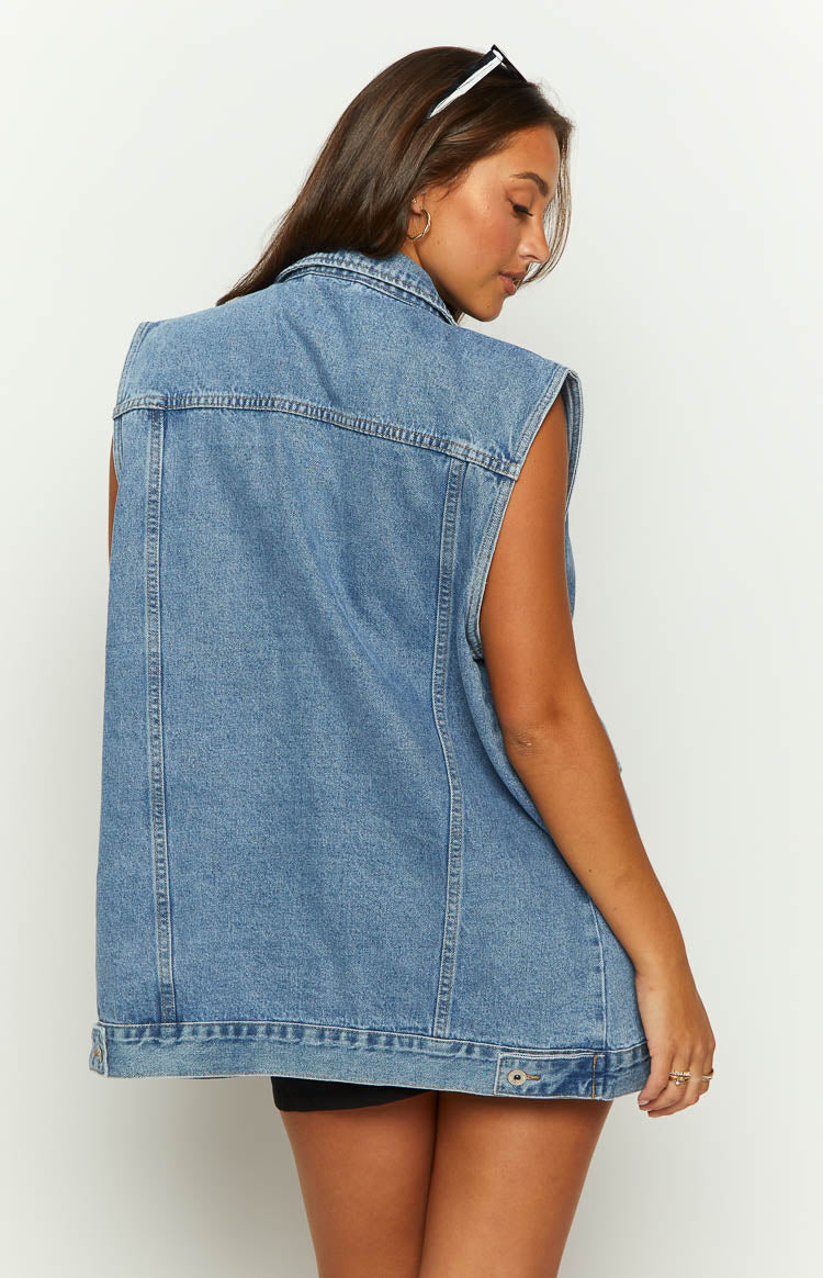 Rear-side view of a mid wash denim vest with a structured back panel and adjustable button tabs at the hem