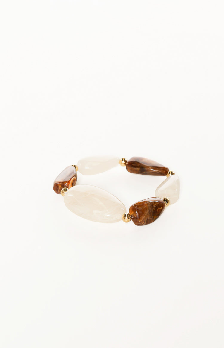 Angled view of an elastic bracelet with alternating brown marbled and milky white resin beads separated by gold spacers