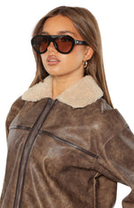 Close-up of black aviator sunglasses with a thick frame and brown tinted lenses, seen from a slight angle