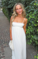White satin maxi dress with a straight neckline, delicate lace trim, thin spaghetti straps, and empire waist