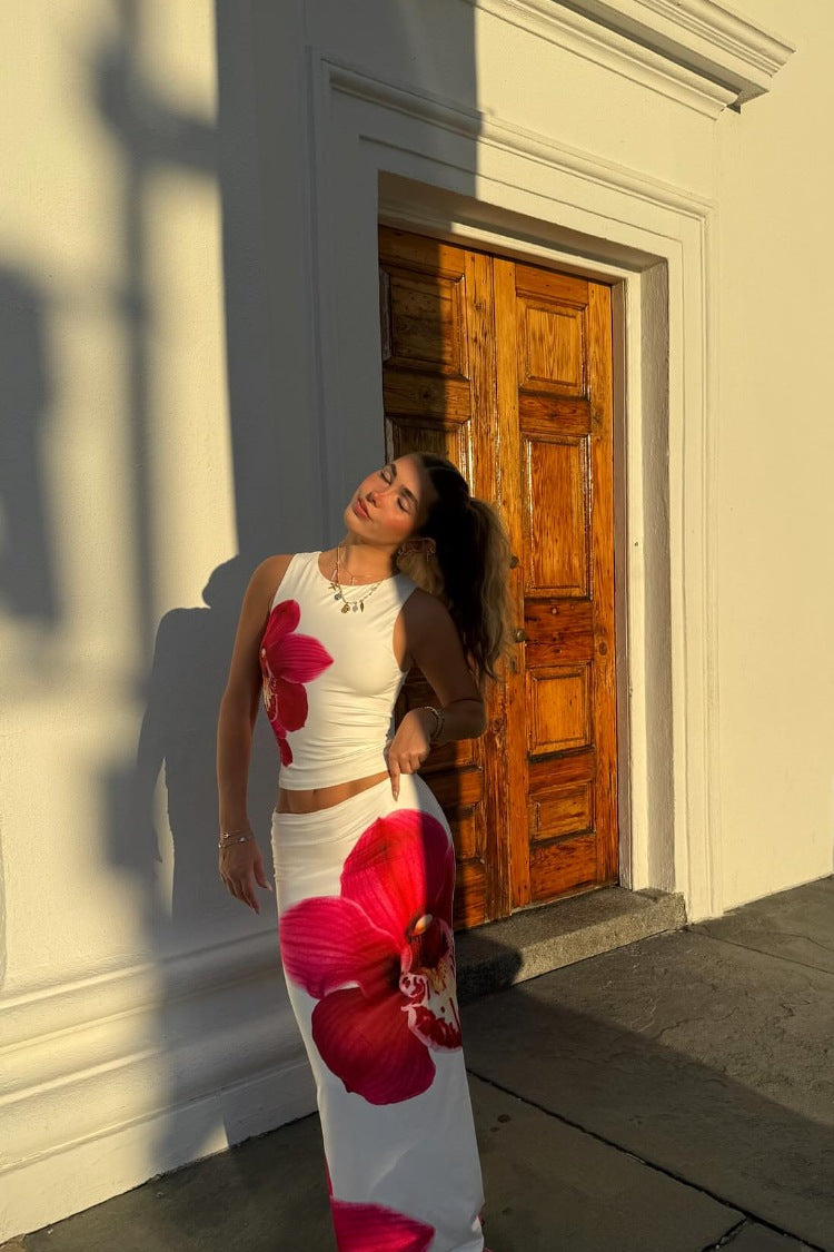 White maxi skirt with a large red orchid print and a low-rise waist, showing its fitted silhouette