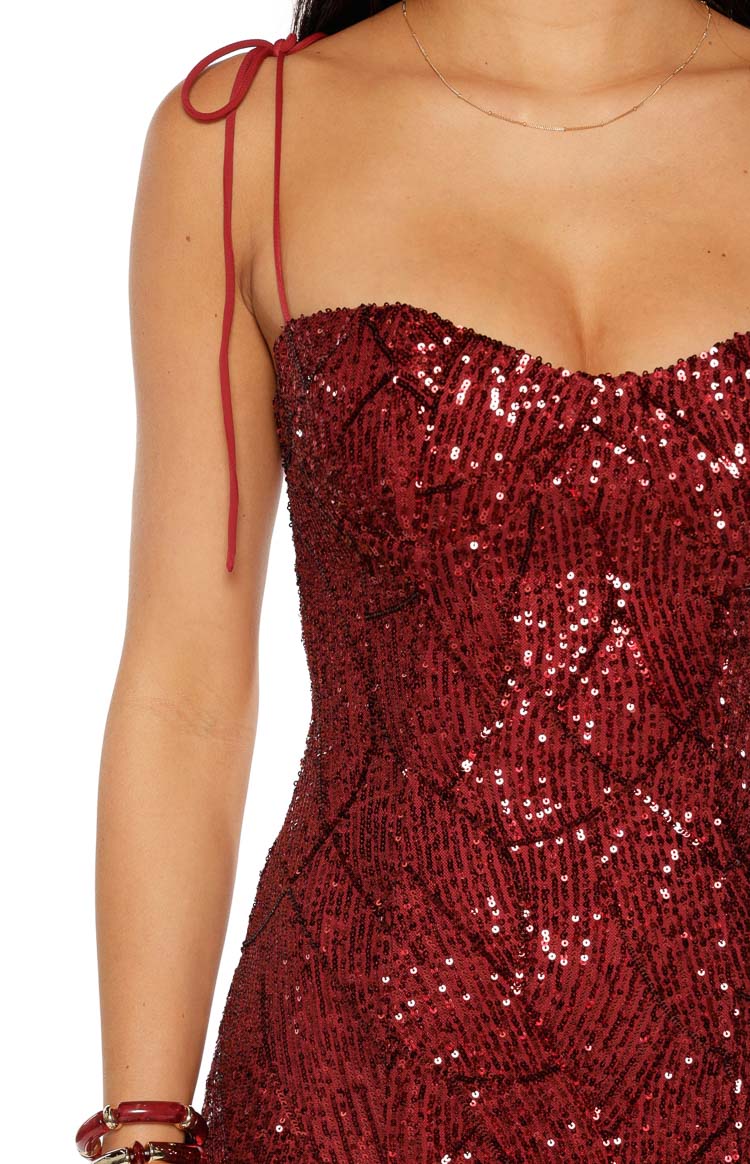 A close-up of a dark red sequin mini-dress highlighting the sweetheart neckline with a quilted sequin pattern and a thin tie-up shoulder strap.