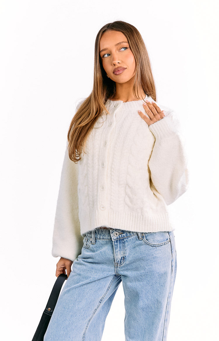Cream cable knit cardigan featuring a round neckline, button-front closure, and ribbed hem