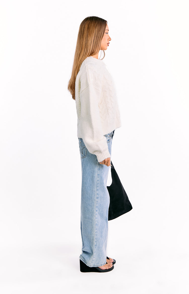 Side view of a cream cable knit cardigan with long, relaxed sleeves and ribbed cuffs