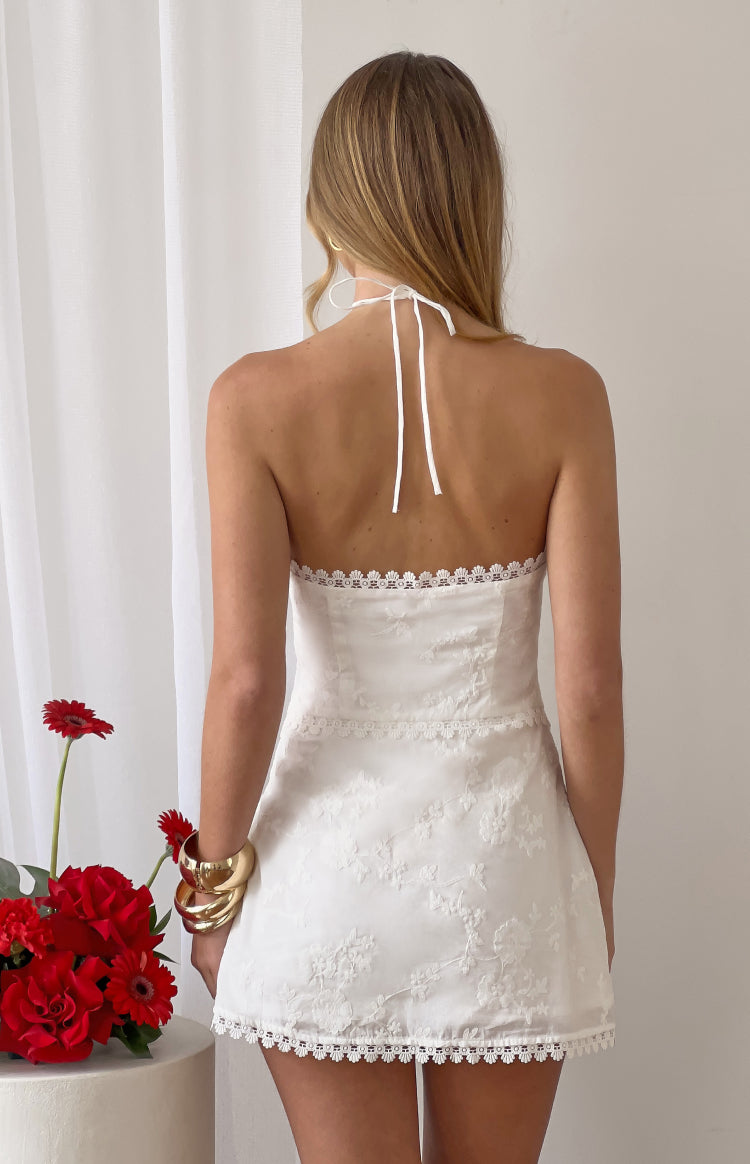 Rear view of a white broderie mini dress with a halter neck tie and scalloped lace trim along the back neckline and waist