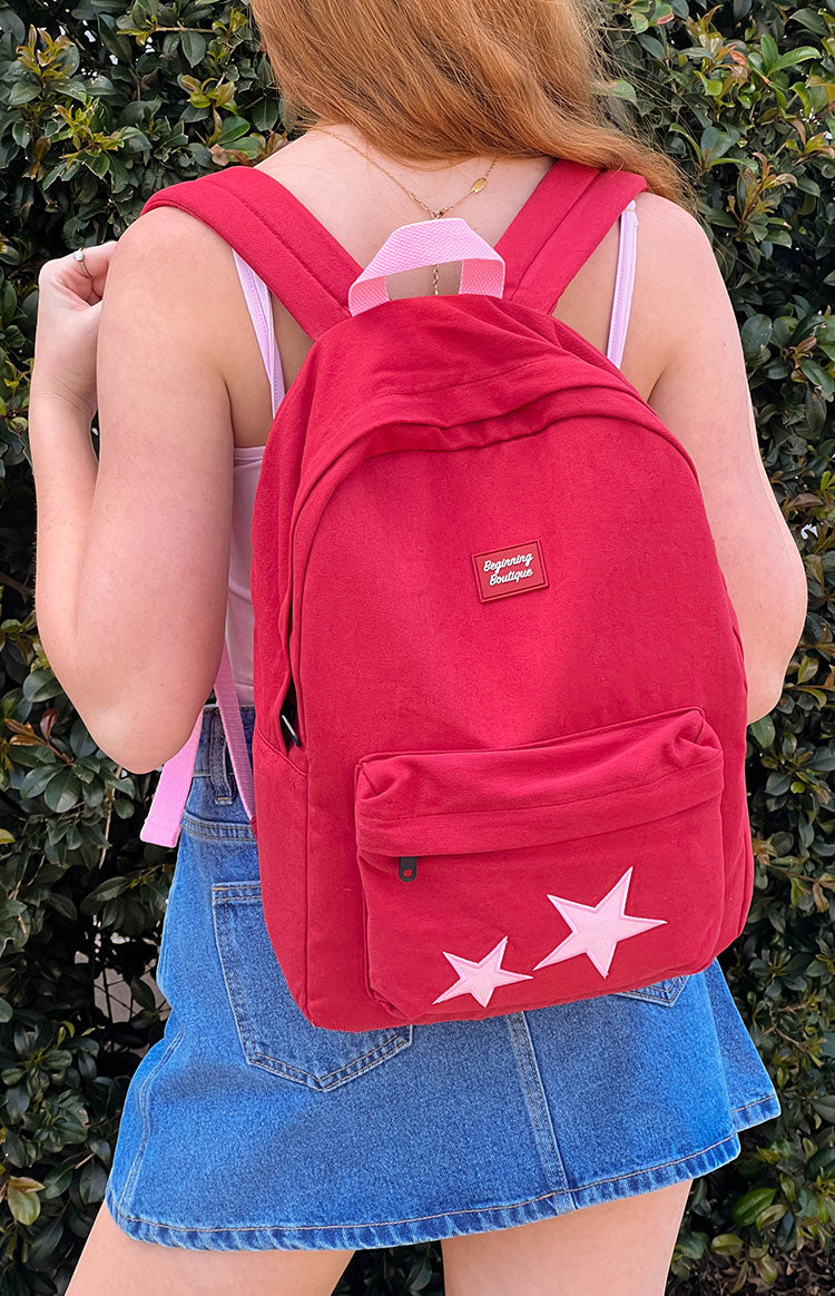 Rear view of a burgundy backpack with two pink star appliques on the front pocket and padded straps