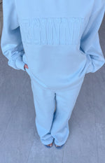 Light blue slouch fit trackpants with wide leg opening, paired with a matching sweatshirt featuring embossed lettering