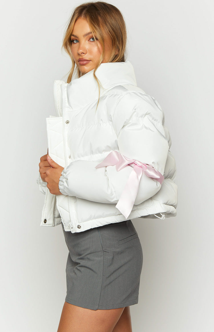 Side view of a white cropped puffer jacket with a high stand collar and a pink satin bow on the sleeve