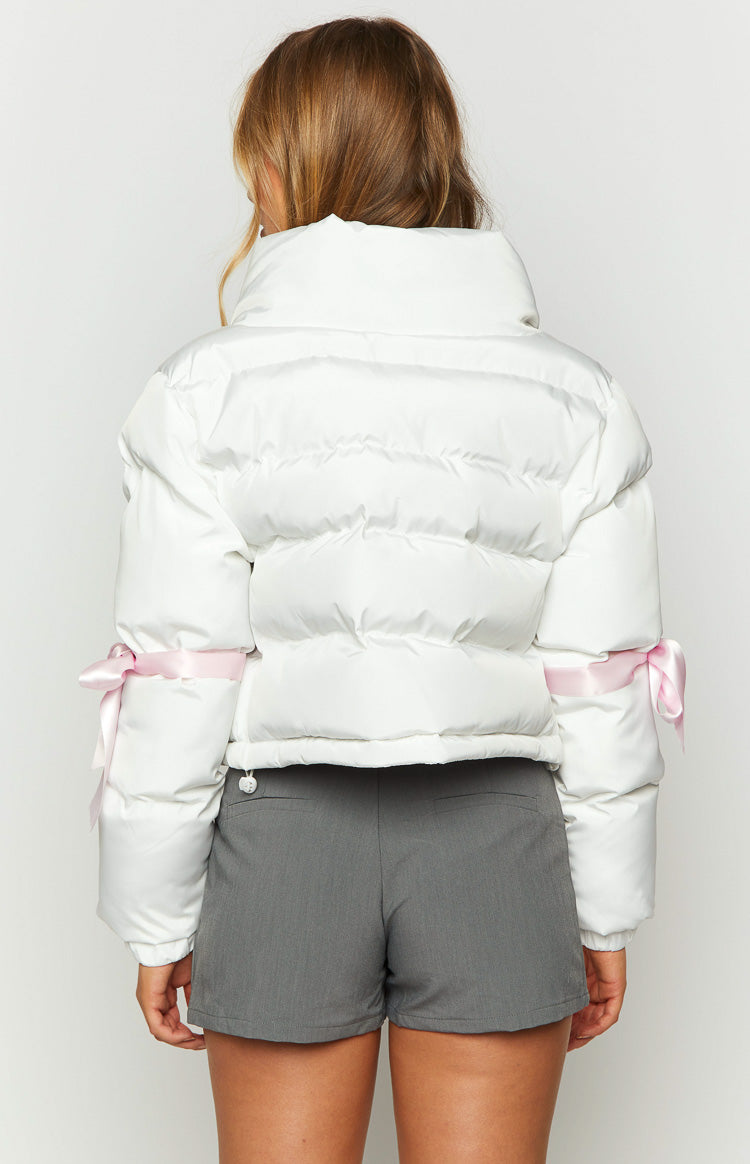 Rear view of a white cropped puffer jacket with a high stand collar and pink ribbon bows tied on the upper sleeves