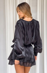 Rear-side view of a black satin mini dress with a gathered scoop back, voluminous long sleeves, tie waist, and tiered skirt