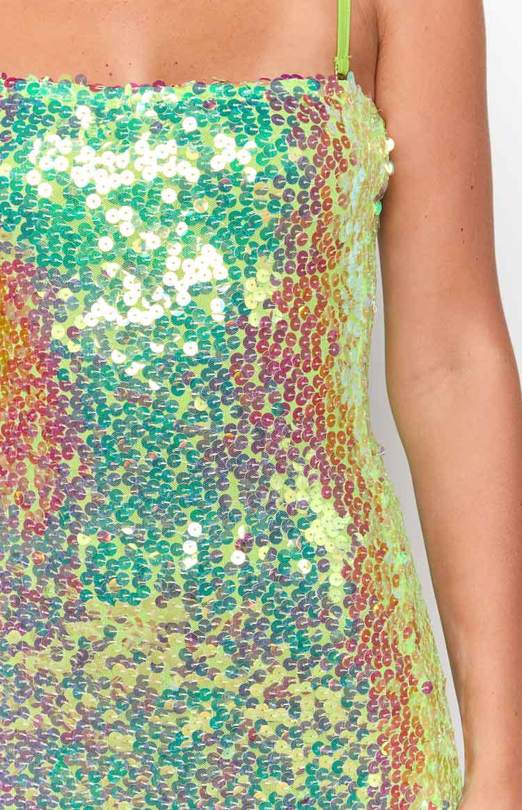 Close-up of the iridescent green, yellow, and pink sequin fabric of the mini dress, with a thin lime green strap