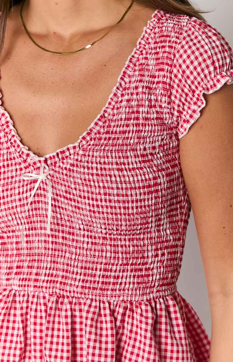 Close-up of the red gingham playsuit showing the shirred bodice, V-neckline with a white bow, and ruffled cap sleeves