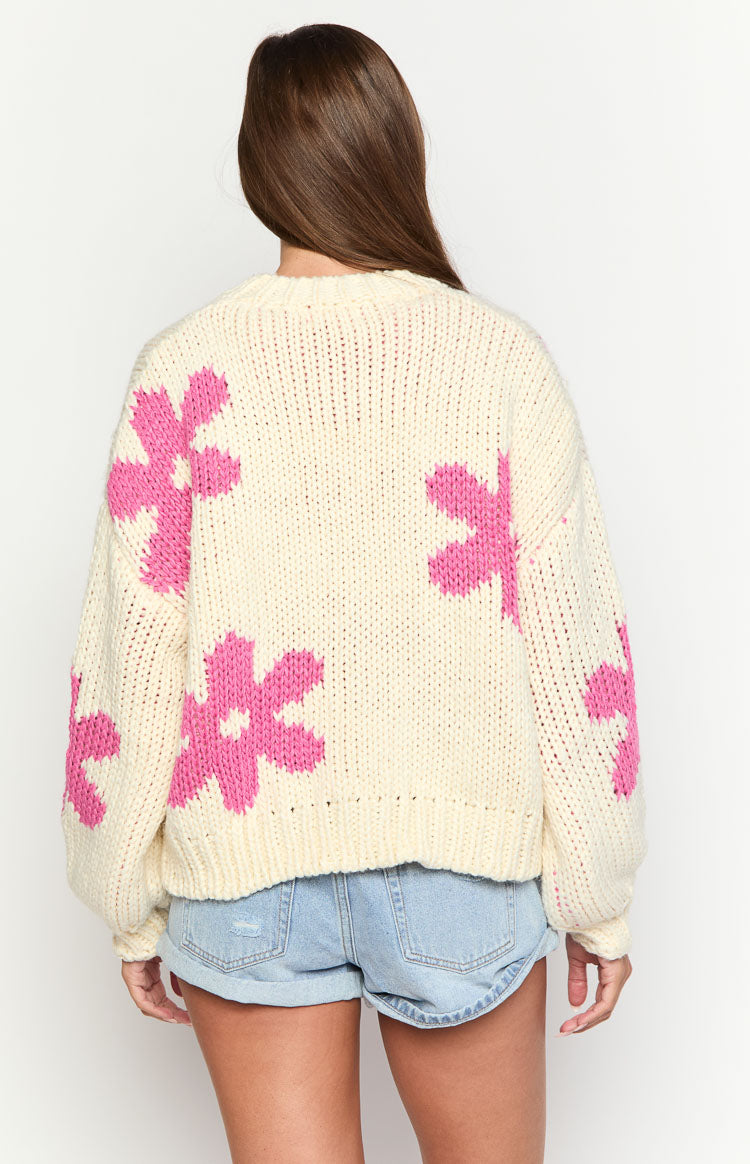 Rear view of an oversized cream knit sweater with large pink flower patterns, long sleeves, and a ribbed hem