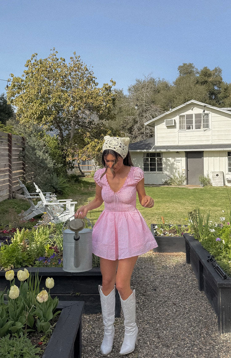 Pink gingham playsuit featuring a smocked bodice, ruffled V-neck, puff sleeves, and a flared hem