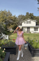 Close-up of the pink gingham playsuit showing the smocked bodice, V-neckline with bow, and ruffled cap sleeves