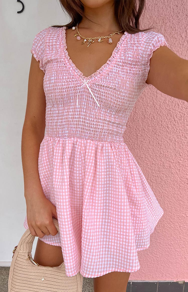 Close-up of the pink gingham playsuit showing the smocked bodice, V-neckline with bow, and ruffled cap sleeves