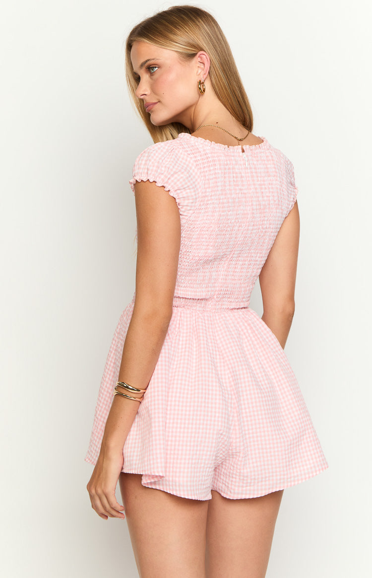 Rear-side view of a pink gingham playsuit showing the smocked back, ruffled cap sleeves, and flared shorts
