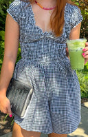 Black gingham playsuit with smocked bodice, V-neck, short puff sleeves, and flared shorts