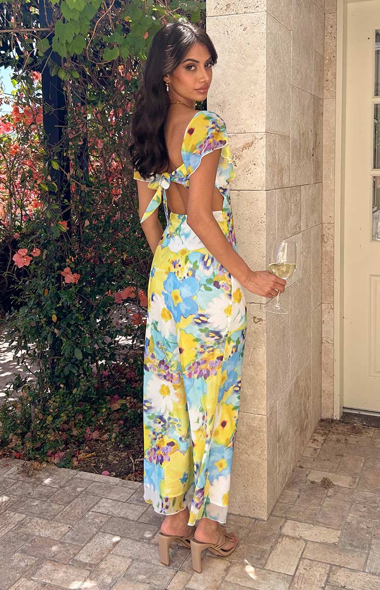 Rear-side view of a blue and yellow floral chiffon maxi dress with a tie-back detail and waist cutouts