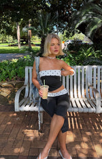Angled front view of a black strapless top with white polka dot bands at the bust and hem, midriff cutout