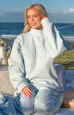 Light blue mock neck sweater with raised BEGINN applique lettering across the chest