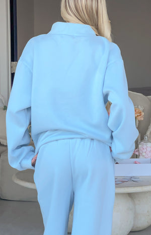 Back view of a light blue mock neck sweater with dropped shoulders and matching relaxed fit track pants