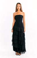 Our female model wearing a black strapless maxi dress with a shirred or smocked bodice and a tiered ruffled skirt.