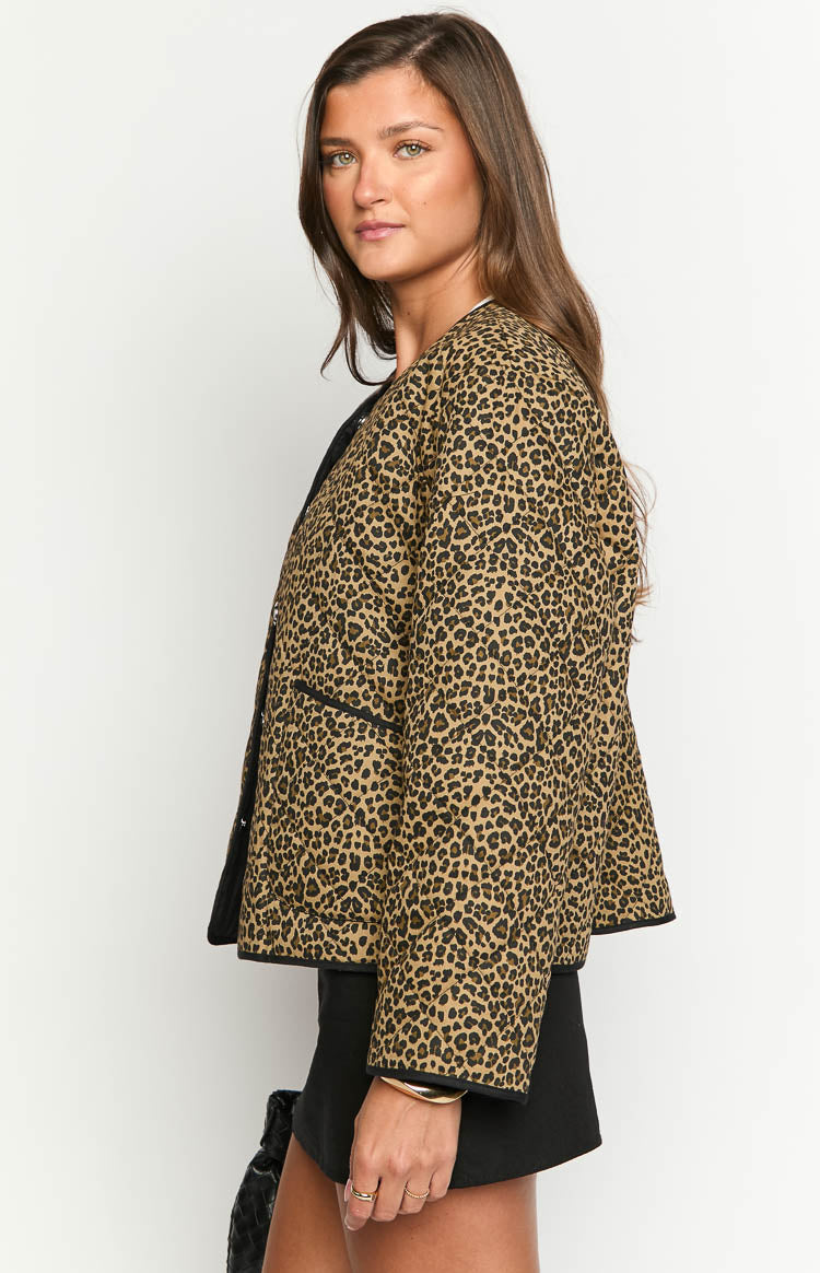 Side view of a leopard print quilted jacket showing black piping detail on the front opening, hem, and faux pockets