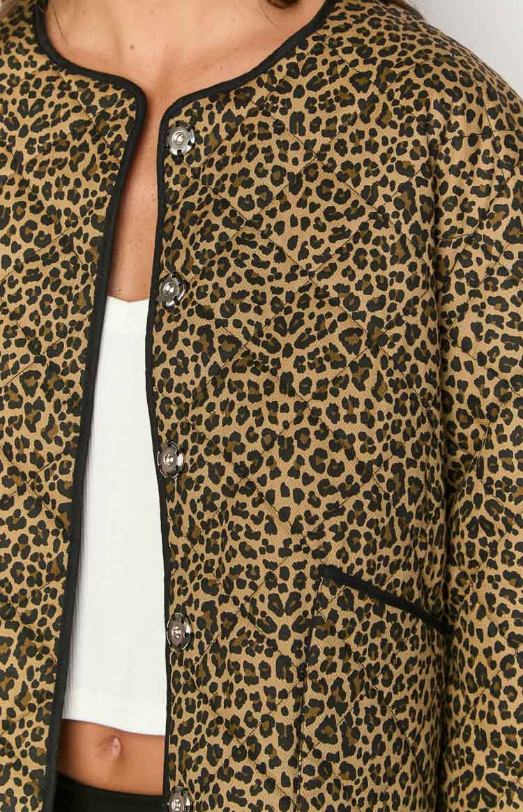 Close-up of the round neckline and silver snap buttons on the leopard print quilted jacket with black piping and diamond quilting