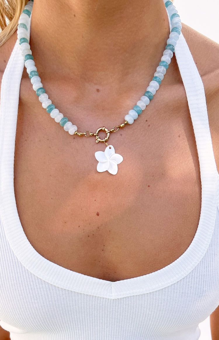 Close-up of the necklace showing alternating light blue and white beads, gold clasp, and white flower charm