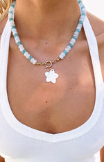 Close-up of the necklace showing alternating light blue and white beads, gold clasp, and white flower charm