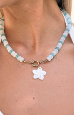 Close-up of the gold toggle clasp and white mother-of-pearl flower charm on a blue and white beaded necklace