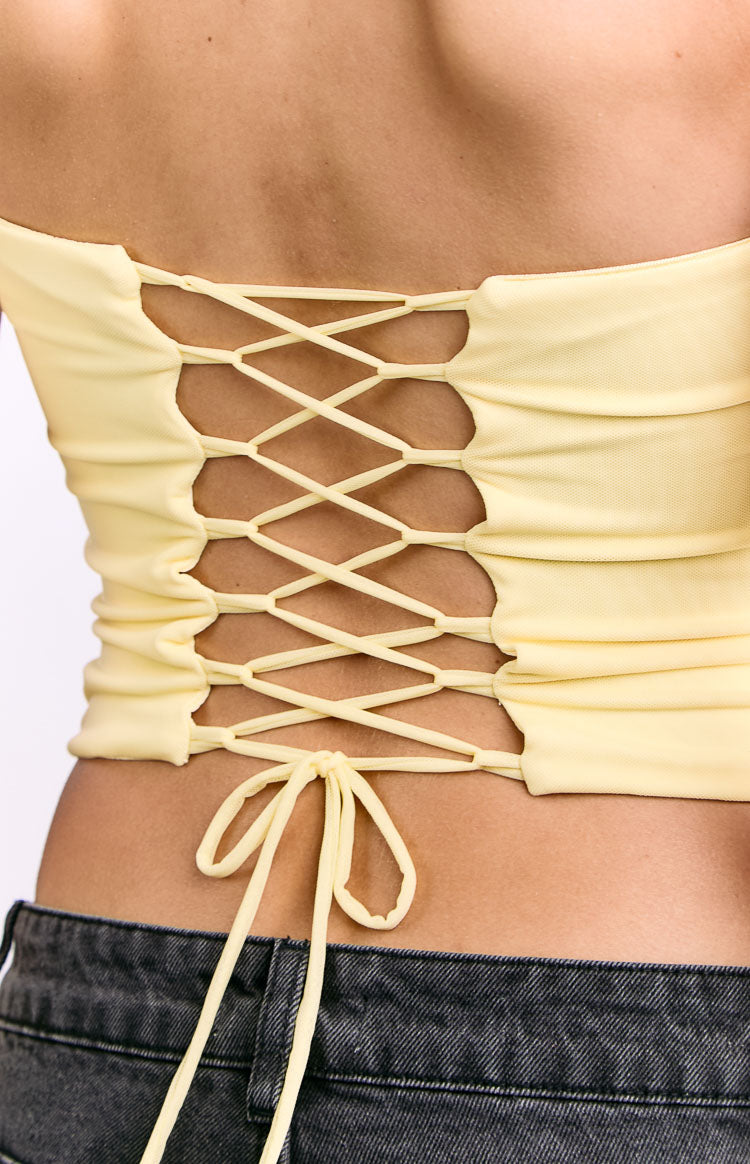Close-up of the back of a yellow corset top with ruched fabric and criss-cross lace-up detail tied at the hem