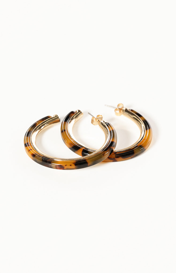 Angled view of two tortoise shell resin hoop earrings showing gold posts and inner metal lining