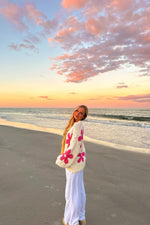 Side view of a cream knit sweater with large pink flower patterns and a relaxed, oversized fit, beach