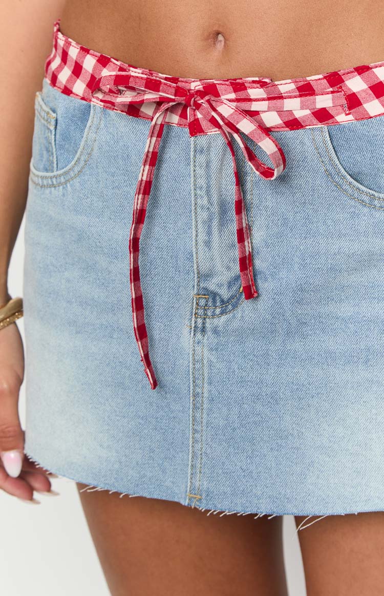 Close-up showing the red and white gingham drawstring waist and frayed hem of a light blue denim mini skirt