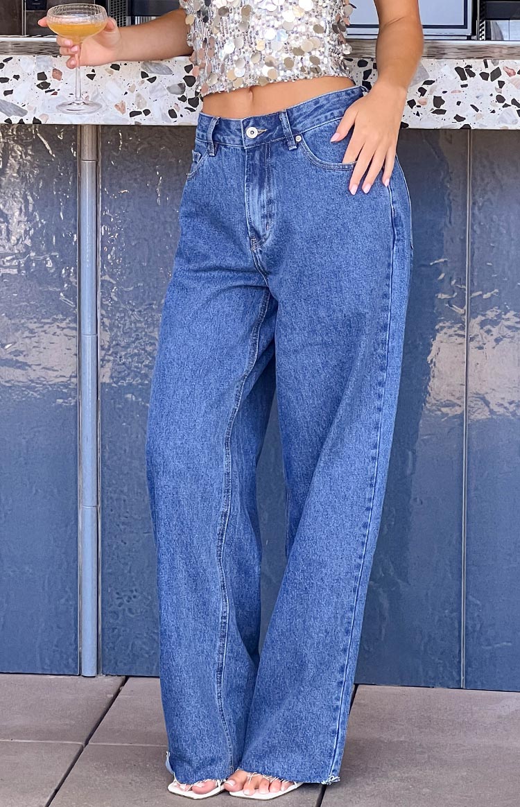 Mid wash wide leg denim jeans featuring a button closure, front pockets, and a frayed raw hem