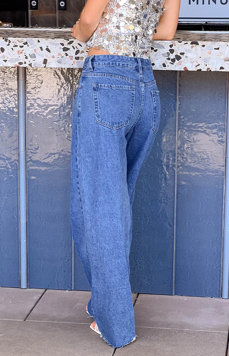 Side-rear view of mid wash wide leg denim jeans with visible back pockets and a raw frayed hem