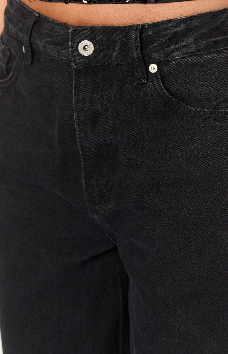 Close-up of the silver button closure and front fly detail on black denim jeans