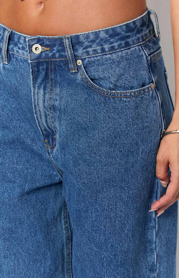 Close-up of the mid-wash denim jeans showing the silver button closure, belt loops, and front pocket