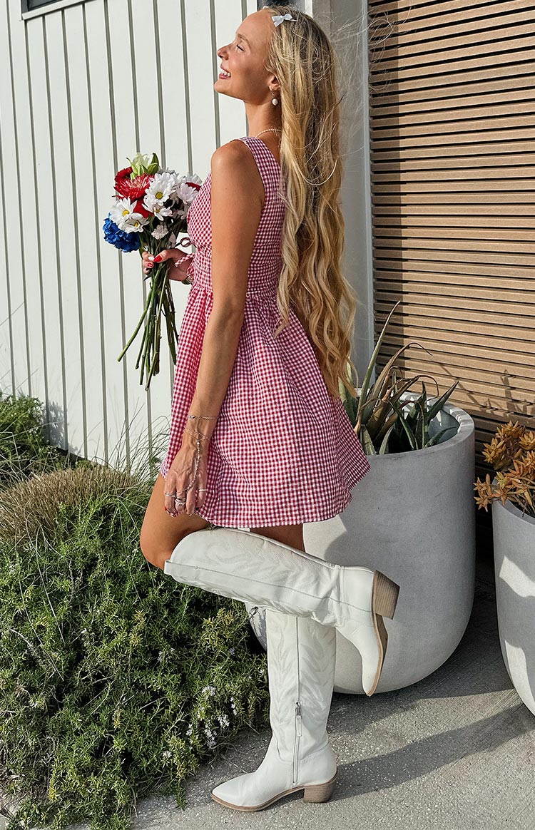 Side profile of a red gingham mini dress with a smocked bodice and a full, flared skirt