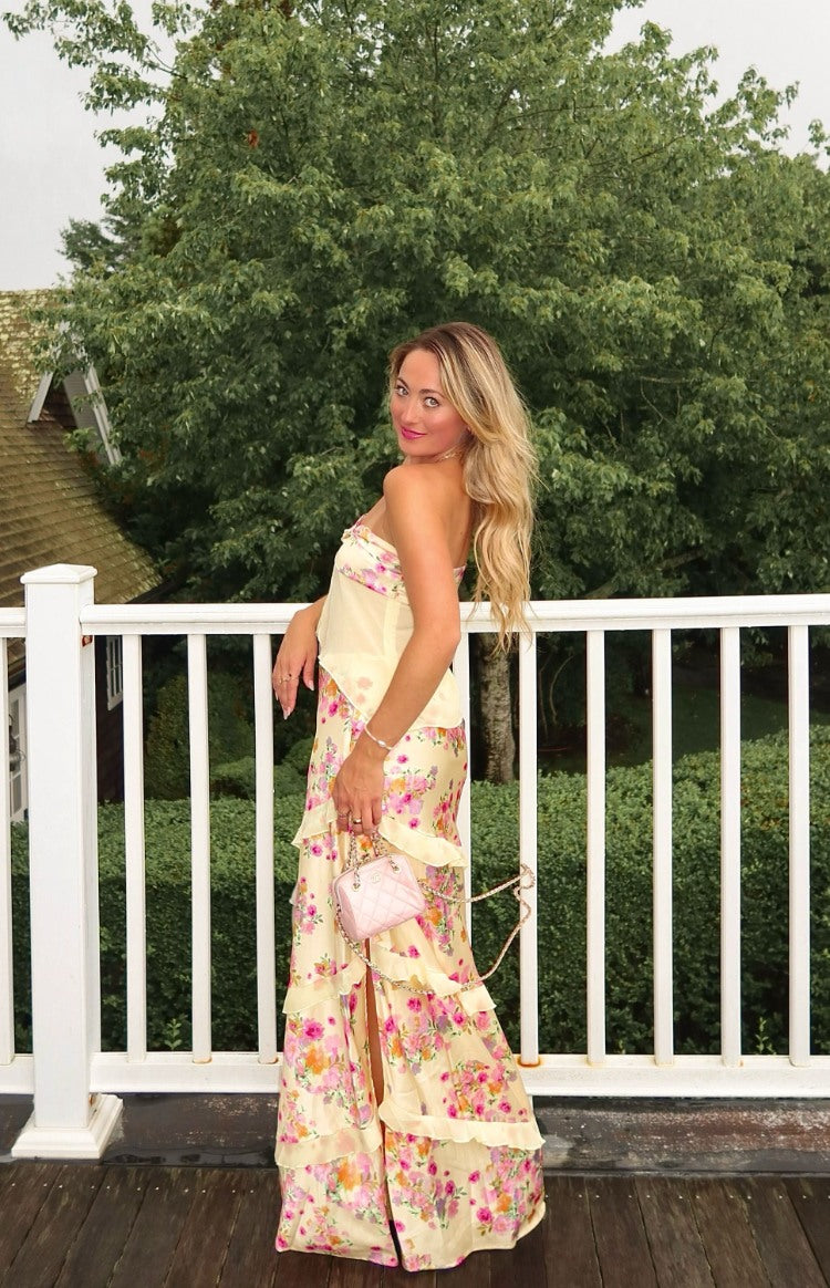 Side angle of a yellow floral maxi skirt featuring yellow chiffon ruffle details. Crafted in a satin material, this maxi skirt is the perfect elegant piece for Wedding Guests and Spring events.