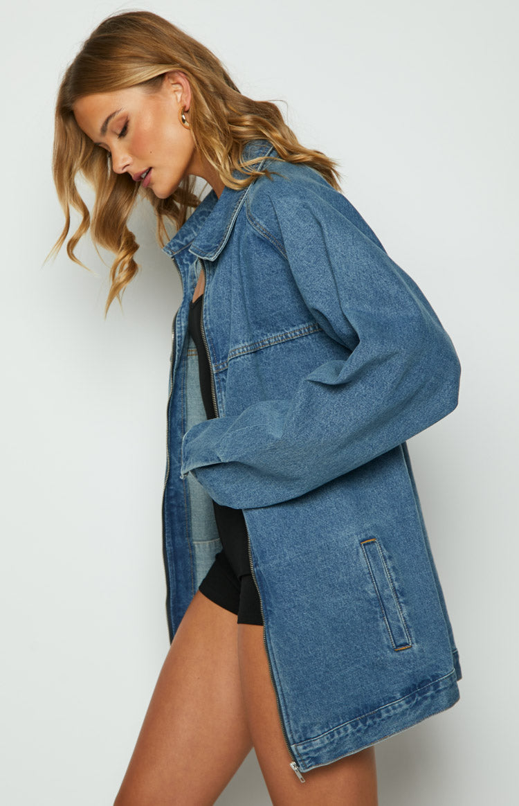 Side view of a blue oversized denim jacket with a collar, long sleeves, and a vertical front pocket detail