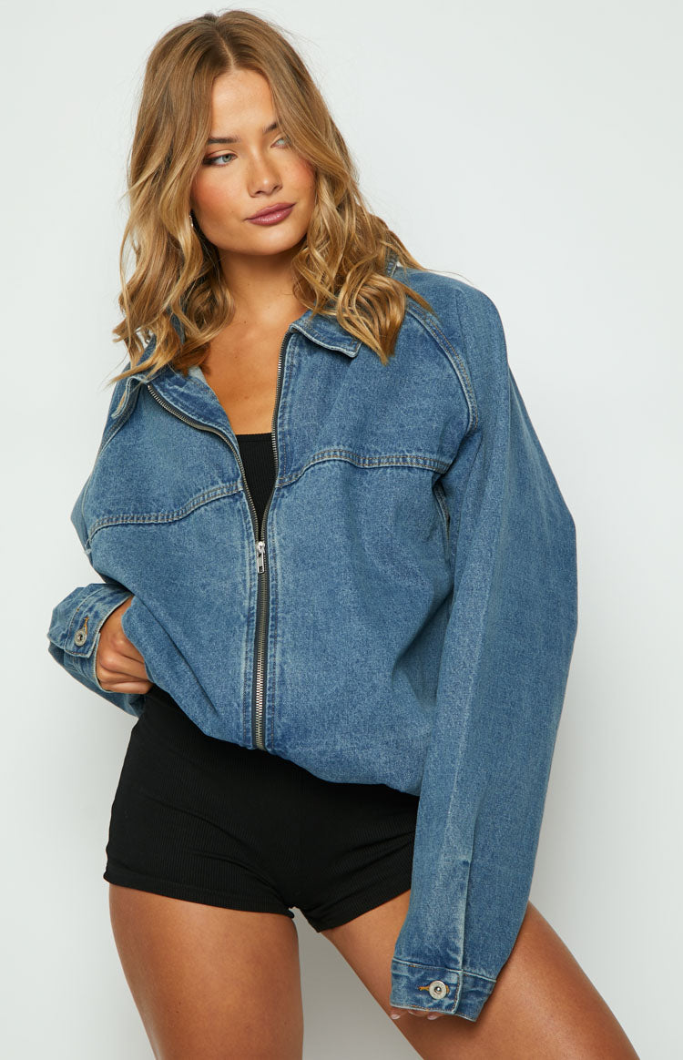 Blue oversized denim jacket with a classic collar, front zipper, dropped shoulders, and buttoned cuffs