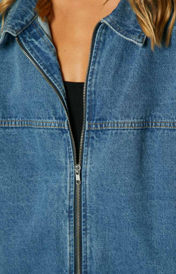 Detail shot of the silver front zipper closure, pointed collar, and orange topstitching on a blue denim jacket