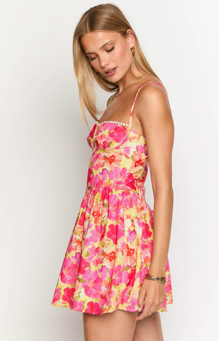 Side view of a yellow floral mini dress with pink flowers, bustier bodice, white pom-pom trim, and gathered skirt