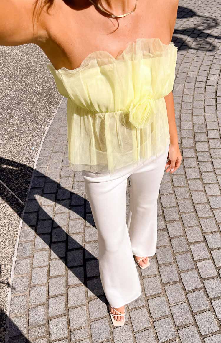 Top-down view of a yellow strapless crop top with ruffled tulle trim and a floral appliqué at the waist