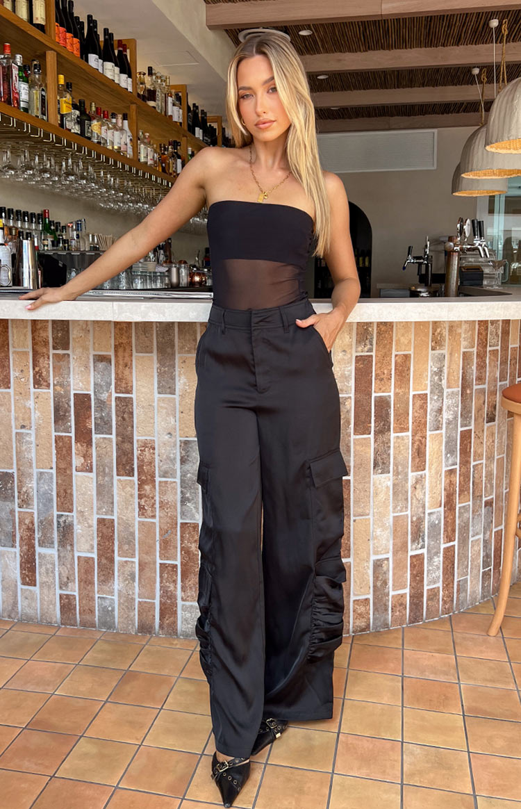 Full length view of black satin cargo pants with wide legs and ruched detail on the lower sides