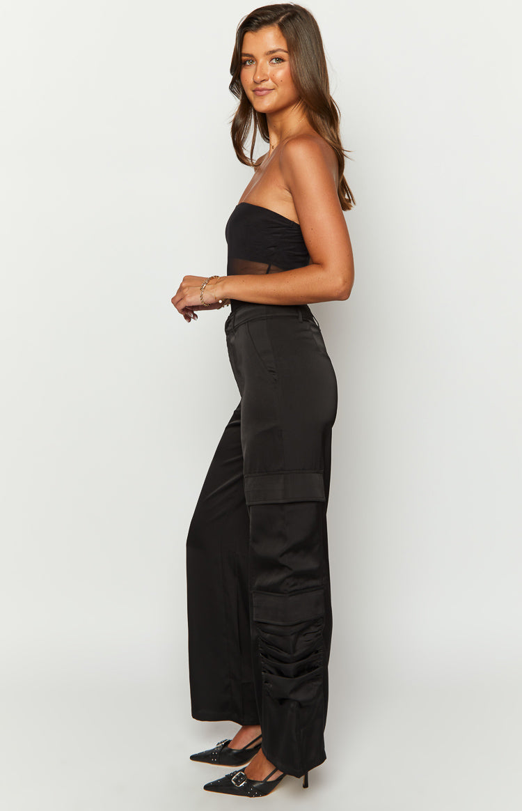 Side view of black satin cargo pants with wide legs and ruched detail on the lower side pockets