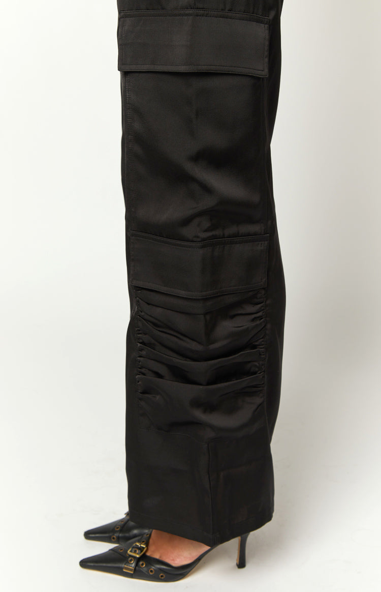 Close-up of black satin cargo pants showing a side flap pocket and ruched detail on the lower leg